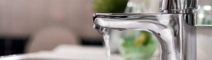 Cold water flowing from faucet in clean bright bathroom